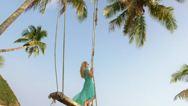 Woman swinging on a swing on a tropical beach, on shores of the turquoise sea