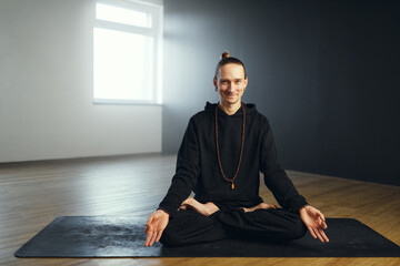 The yogi man sits on the mat in the lotus position with gyan mudra. Yoga practice in the studio.