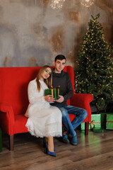 Obraz premium Man and woman sitting on a red sofa and holding a gift