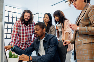 multiracial group of creative workers pay attention to the work of a colleague on his laptop....
