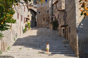 A woman is walking up the stairs among ancient stone buildings in the medieval town Sermoneta in Italy