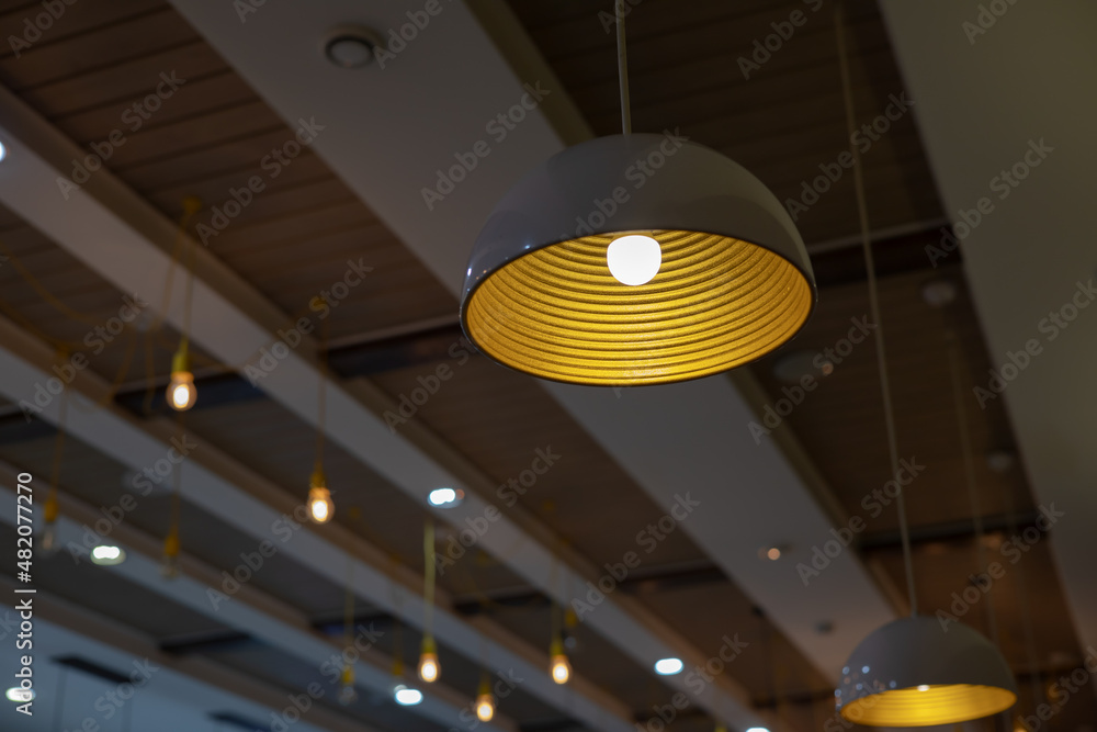 Poster a lampshade with a glowing lamp hangs on the ceiling in the cafe against the background of other lig