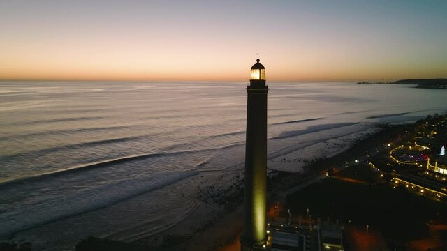 Beautiful Maspalomas lighthouse at night. The working beacon at Gran Canaria island. Flight around the working pharos at night. Canary islands light house. Spain. Citylights of Maspalomas.
