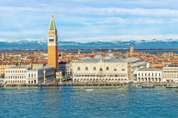 Fototapeta premium Blick von der Chiesa di San Giorgio Maggiore auf die Piazza San Marco mit dem Campanile di San Marco und den Palazzo Ducale in Venedig mit schneebedeckten Alpen im Hintergrund