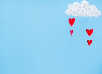 Fototapeta na wymiar White clouds and red paper hearts in the form of rain on a blue background. Abstract background with paper-cut shapes. Sainte Valentine, mother's day, birthday greeting cards, invitation