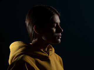 Fototapeta na wymiar Relaxation and meditation, a young brunette woman, side view, light silhouette on a dark studio background. Calm face, the importance of mindfulness for young people