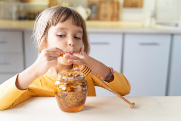 Child girl eating golden honeycomb and beeswax in a jar of honey on the table. Fresh organic honey...