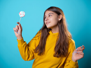 Beautiful young brunette with a lollipop in her hands, sweet candy, portrait in yellow on a blue background, bright colors