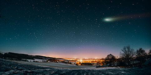 Panorama of the night sky with a comet. Winter night landscape with city lights on the horizon