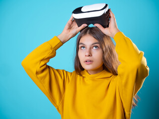 Immersion in a virtual 3D world, a young woman in a youth outfit uses a virtual reality helmet. A brunette in yellow on a blue background puts a vr gadget on her head