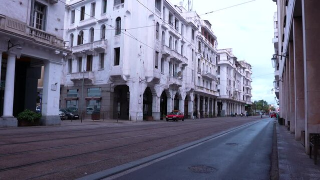 Tramway passes through buildings with city hall in background on a cloudy day.