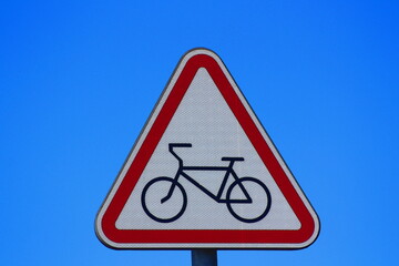 The road sign of the bicycle path is triangular in shape with the image of a bicycle against the sky.