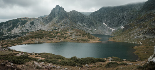 Amazing panoramic view of Twins glacier lake on Rila mountain, dog on a rock, pointy peaks and dramatic sky