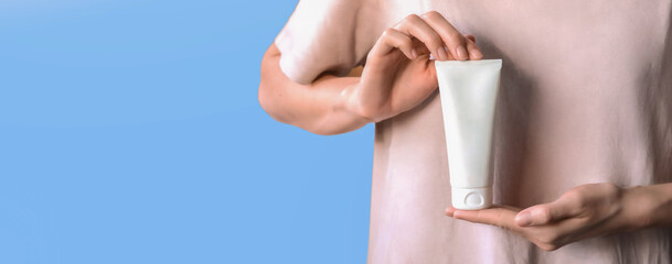 Skin moisturising concept. Top above overhead pov first person view photo of female hands holding white tube of cream isolated on pastel blue background with copyspace.