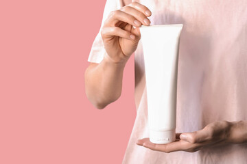 Skin moisturising concept. Top above overhead pov first person view photo of female hands holding white tube of cream isolated on pastel pink background with copyspace.