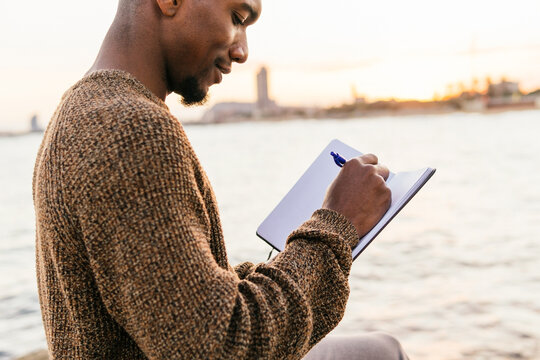 Black man writing in notebook on embankment