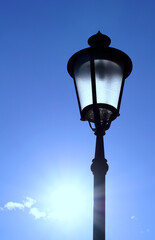 Fototapeta na wymiar A street lamp made of black metal on a background of blue sky with the sun shining