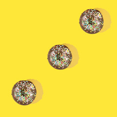Three chocolate donuts with sprinkles, on yellow background