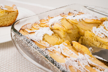 Fresh baked apple cake with biscuit base close up in glass baking dish on kitchen table