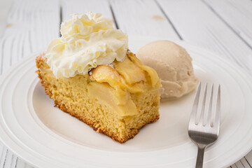 Piece of apple cake with biscuit base and whipped cream topping, served with vanilla ice cream close up on a plate on wooden background