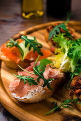 Bruschetta with prosciutto, cheese, tomatoes, herbs on a wooden board. Tasty breakfast.
