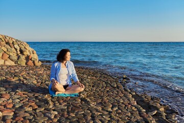 Mature woman sitting in lotus position meditating on the beach.