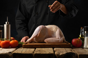 The chef in a black uniform sprinkles salt on a whole carcass of chicken, turkey. Ingredients....
