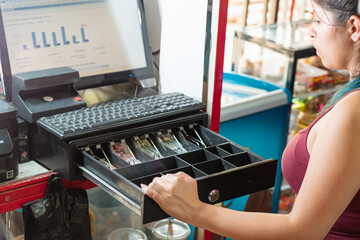latina woman looking disappointed at the cash register of her business to see how much money there...