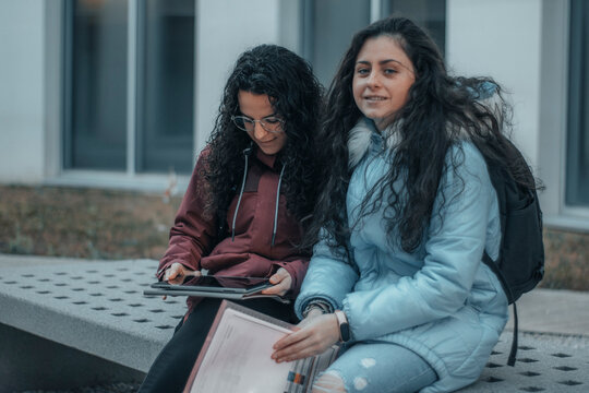 Chicas jovenes estudiantes sentadas en el campus universitario revisando sus tareas y apuntes escolares para estudiar en su hora de descanso