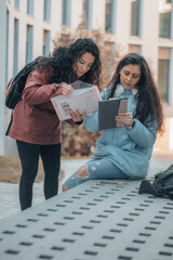 Jovenes alumnas de la facultad universitaria comentando un tema junto con apuntes y una tablet en el descanso de clases del centro universitario para aprobar el examen 