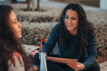 Muchacha joven alumna sonriente estudiando para el examen en el descanso de su centro universitario junto con una compañera de trabajo para finalizar su tarea