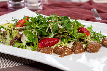 Salad with chicken liver and strawberry on a white plate