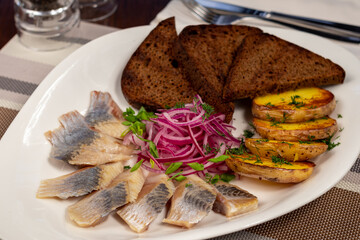 Herring with potatoes, red onion and black bread on white plate