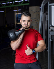 Fototapeta na wymiar Athletic man in a red shirt holding kettlebell in his hand for strength workout at the gym
