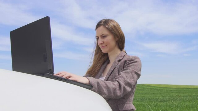 Bussinesswomanl with a laptop on a car, alone in a green field. Freedom, business, work from anywhere and social distancing concept.