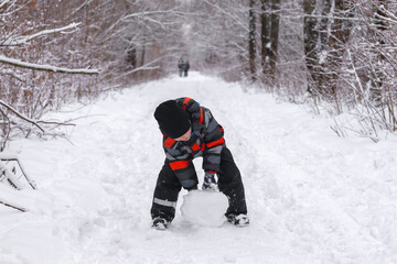 Fototapeta na wymiar boy making a snowman in winter park