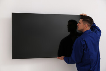 Professional technician installing modern flat screen TV on wall indoors