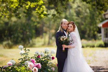 Wedding day of Young couple in a summer garden. Bride and Groom tender holding each other. Redhead woman and blonde man with long hairs. Wedding family outdoor walk. Love and tenderness