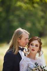 Wedding day of Young couple in a summer garden. Bride and Groom tender holding each other. Redhead woman and blonde man with long hairs. Wedding family outdoor walk. Love and tenderness