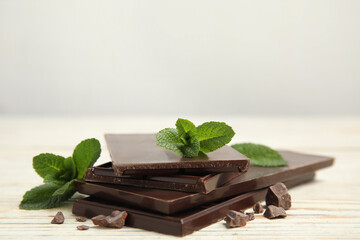 Tasty dark chocolate pieces with mint on white wooden table