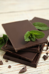 Tasty dark chocolate pieces with mint on white wooden table, closeup