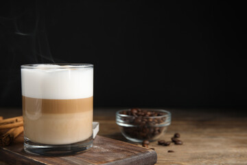 Delicious latte macchiato, cinnamon sticks and coffee beans on wooden table, space for text