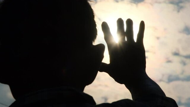 Silhouette of a senior man reaching out to the evening sunlight. Hands of a happy senior man at sunset.