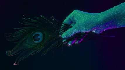 Female hand covered with holographic shining glitter holding peacock feather under neon colored light. Body art, glamorous conceptual footage, fashion style. - Powered by Adobe