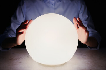Businesswoman using glowing crystal ball to predict future at table in darkness, closeup. Fortune...