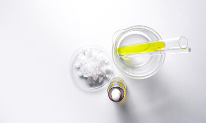Sea Salt in Chemical Watch Glass and Nickle chloride liquid in test tube place next to Dropper Bottle with Yellow cosmetic liquid. Top View