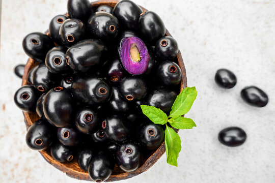 Black ripe Syzygium cumini fruits. Dark black java plum in a wood bowl at isolated white background. Green mint leaf on top of some large java plums.