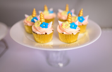 Unicorn-themed 6 beautiful cupcakes on the stand, birthday party sweets close up. Icing unicorn horn and flowers on top of cupcakes.