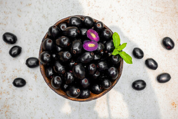 Dark pink-red ripe Syzygium cumini fruits. Dark black java plum in a wood bowl at isolated white...