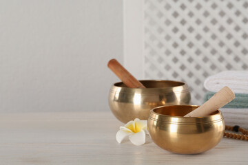 Golden singing bowls, mallets and flower on white wooden table, space for text